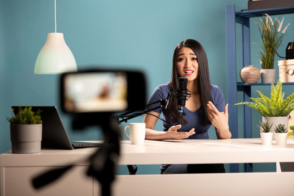 Mulher apresentando conte&uacute;do em est&uacute;dio com microfone e c&acirc;mera, criando estrat&eacute;gias de marketing promocional digital.