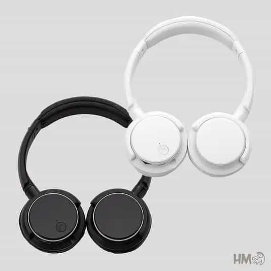 Dois fones de ouvido de modelo supra-auricular (headset) dispostos diagonalmente em um fundo cinza claro. Um par é na cor preta e o outro na cor branca. Ambos possuem design minimalista, acabamento fosco e hastes ajustáveis. No canto inferior direito, há um pequeno logotipo cinza com as iniciais "HM".