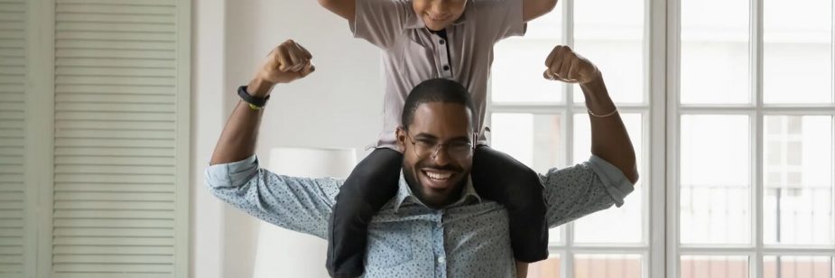 Pai com filhos nos ombros, ambos fazendo uma pose com os braços flexionados para cima, demonstrando força