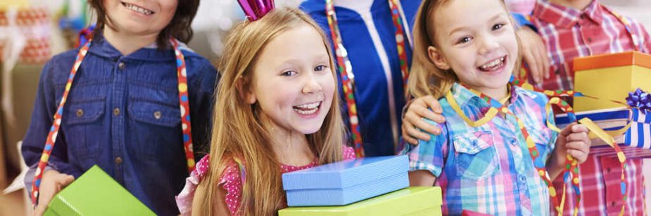Crianças com enfeites com chapeuzinho, lacinho e fitas decorativas, celebrando segurando caixas de presente que simbolizam lembrancinha para alunos
