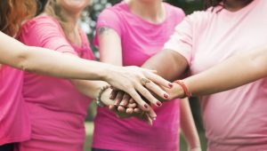 mulheres usando camisetas rosas e juntando as mãos representando ideias para outubro rosa na empresa