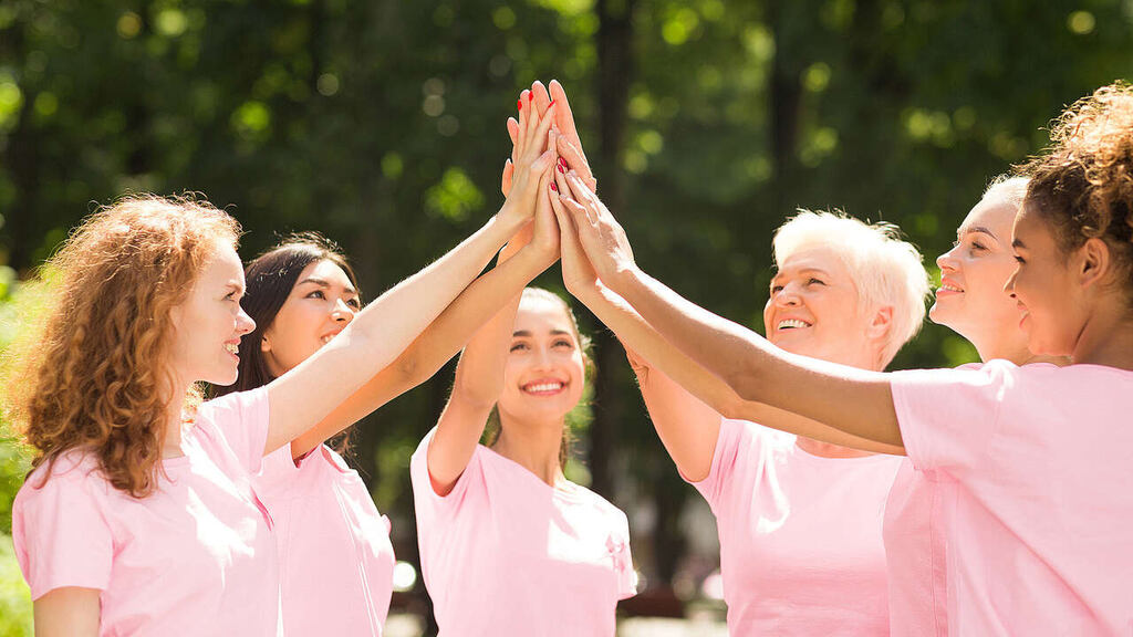 mulheres com blusas rosas unindo as mãos em evento da empresa representando ideias para outubro rosa na empresa