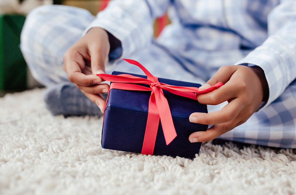 homem embrulhando presente em embalagem azul com fita vermelha para lembracinha para o dia das crianças