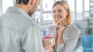 Mulher sorridente recebendo um presente, com expressão de surpresa e alegria, lembrança dia da mulher empresa.