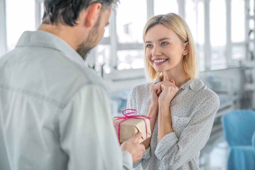 Mulher sorridente recebendo um presente, com expressão de surpresa e alegria, lembrança dia da mulher empresa.