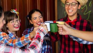 Grupo de amigos com trajes juninos brindando com canecas, cenário festivo associado a lembrancinhas para as festas juninas.
