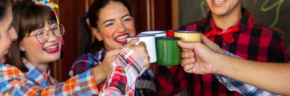 Grupo de amigos com trajes juninos brindando com canecas, cenário festivo associado a lembrancinhas para as festas juninas.