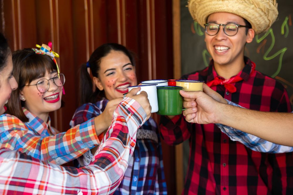 Grupo de amigos com trajes juninos brindando com canecas, cenário festivo associado a lembrancinhas para as festas juninas.