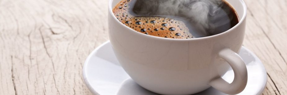 Xícara branca com café quente soltando vapor sobre mesa de madeira, referência visual para frases para xícaras de café simples e acolhedoras.