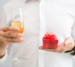 Pessoa segurando taça de champagne e uma caixa vermelha com brindes inovadores.