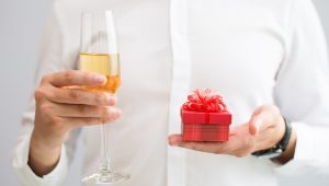 Pessoa segurando taça de champagne e uma caixa vermelha com brindes inovadores.