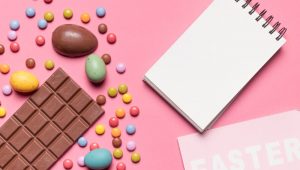 Chocolate, balas coloridas e ovos de Páscoa dispostos com um bloco de notas vazio, perfeito para um presente de Páscoa para funcionários.