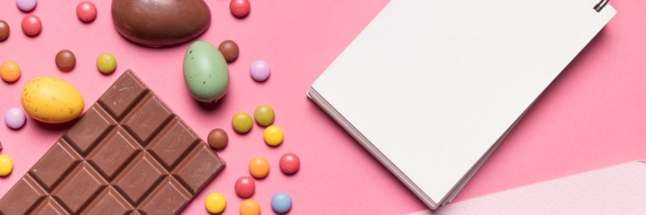 Chocolate, balas coloridas e ovos de Páscoa dispostos com um bloco de notas vazio, perfeito para um presente de Páscoa para funcionários.