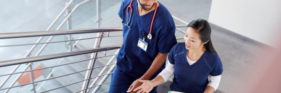 Dois profissionais de enfermagem em uniforme conversando em ambiente hospitalar, representação do impacto dos brindes para enfermagem em ações de reconhecimento.
