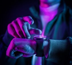 Pessoa ajustando um smartwatch com iluminação neon colorida, demonstrando tecnologia wearable moderna em um ambiente escuro.