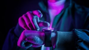 Pessoa ajustando um smartwatch com iluminação neon colorida, demonstrando tecnologia wearable moderna em um ambiente escuro.