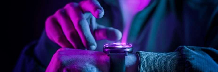 Pessoa ajustando um smartwatch com iluminação neon colorida, demonstrando tecnologia wearable moderna em um ambiente escuro.