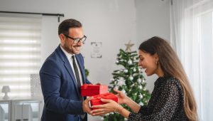 Homem entregando presentes para colega em um escritório decorado para o Natal, demonstrando uso de brindes corporativos em datas comemorativas.