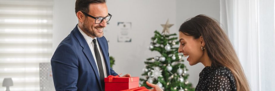 Homem entregando presentes para colega em um escritório decorado para o Natal, demonstrando uso de brindes corporativos em datas comemorativas.